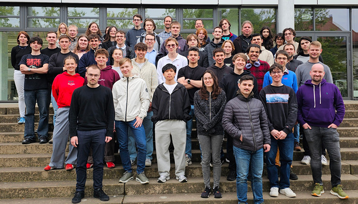 Gruppe junger Menschen posing vor gläsernem Gebäudefront auf Treppenstufen.